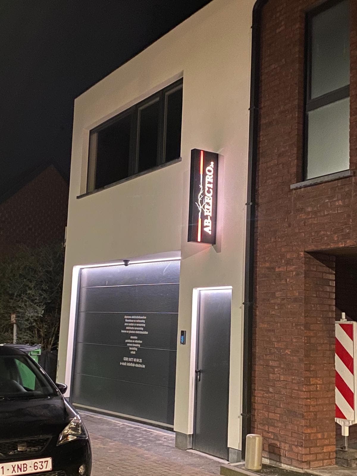 Het pand van AB-Electro in Aalst met verlicht uithangbord 's avonds